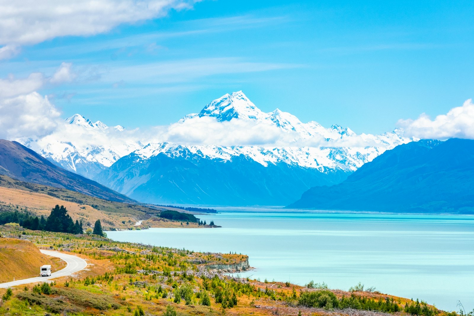 A motorhome on the highway below Aoraki / Mount Cook and the turquoise water of Lake Pukaki — touring New Zealand in a rental campervan