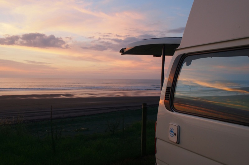 A campervan freedom-camping at a beach at sunset