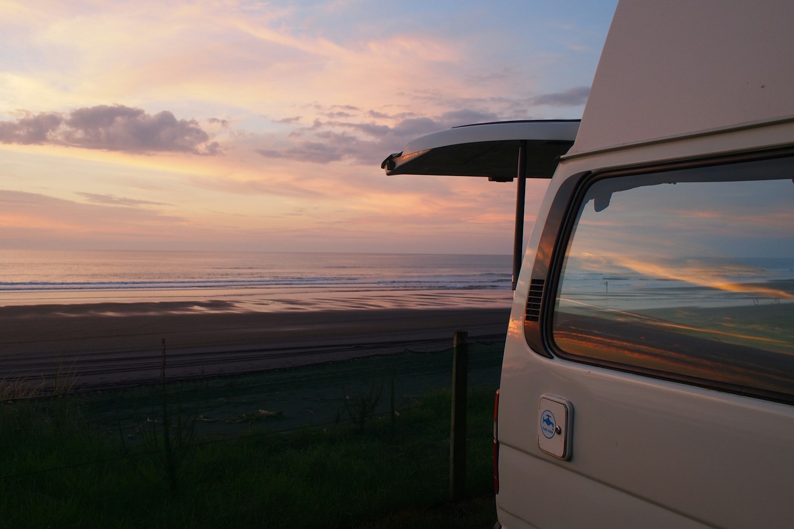 A self-contained campervan freedom-camping at a black-sand beach at sunset in New Zealand