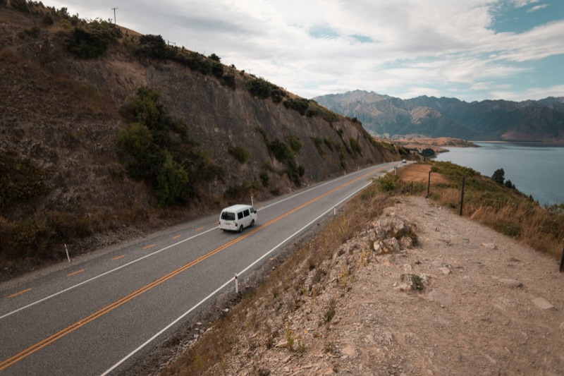 A campervan on a winding lakeside New Zealand highway