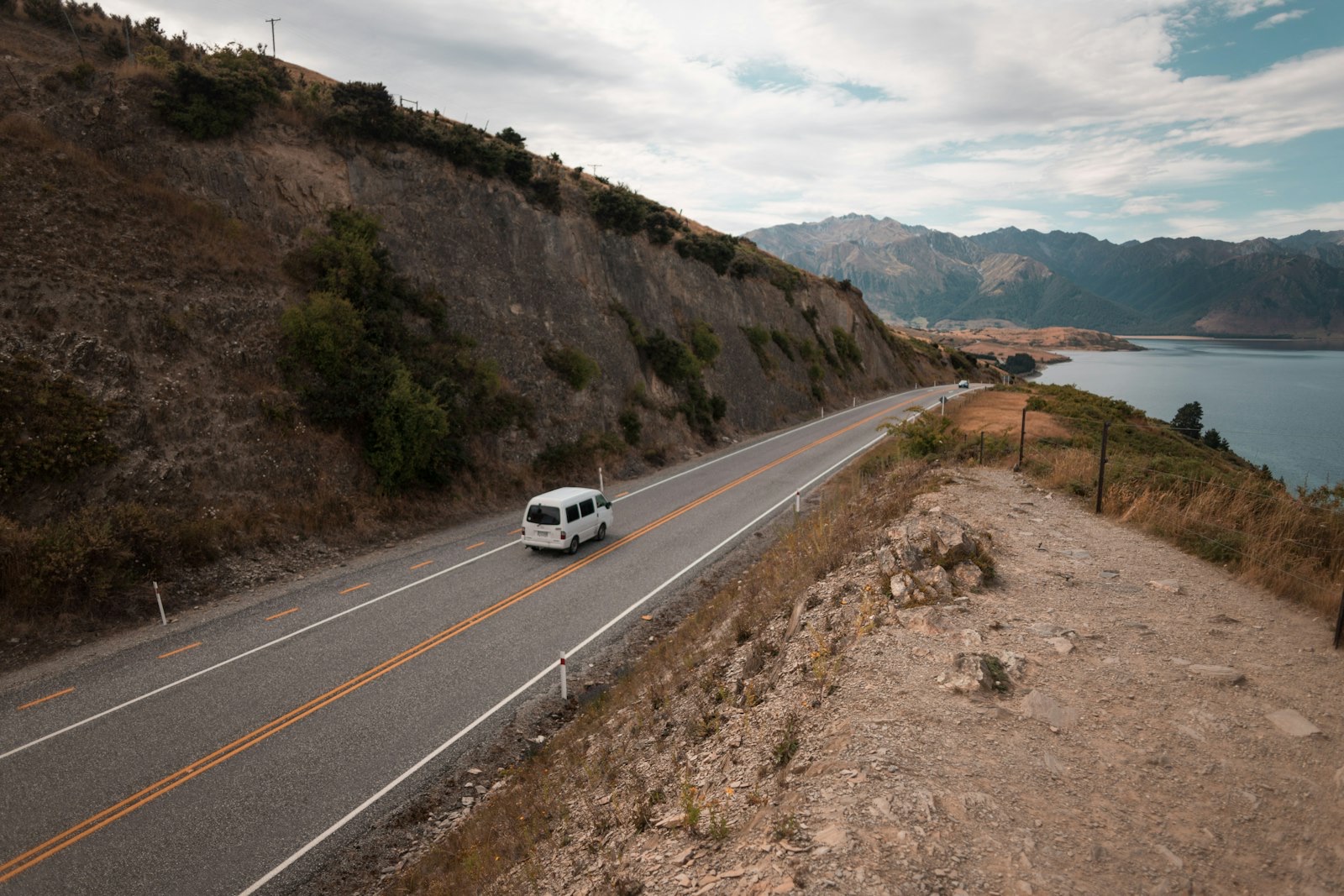 A campervan on a winding lakeside highway in the South Island — touring New Zealand by road